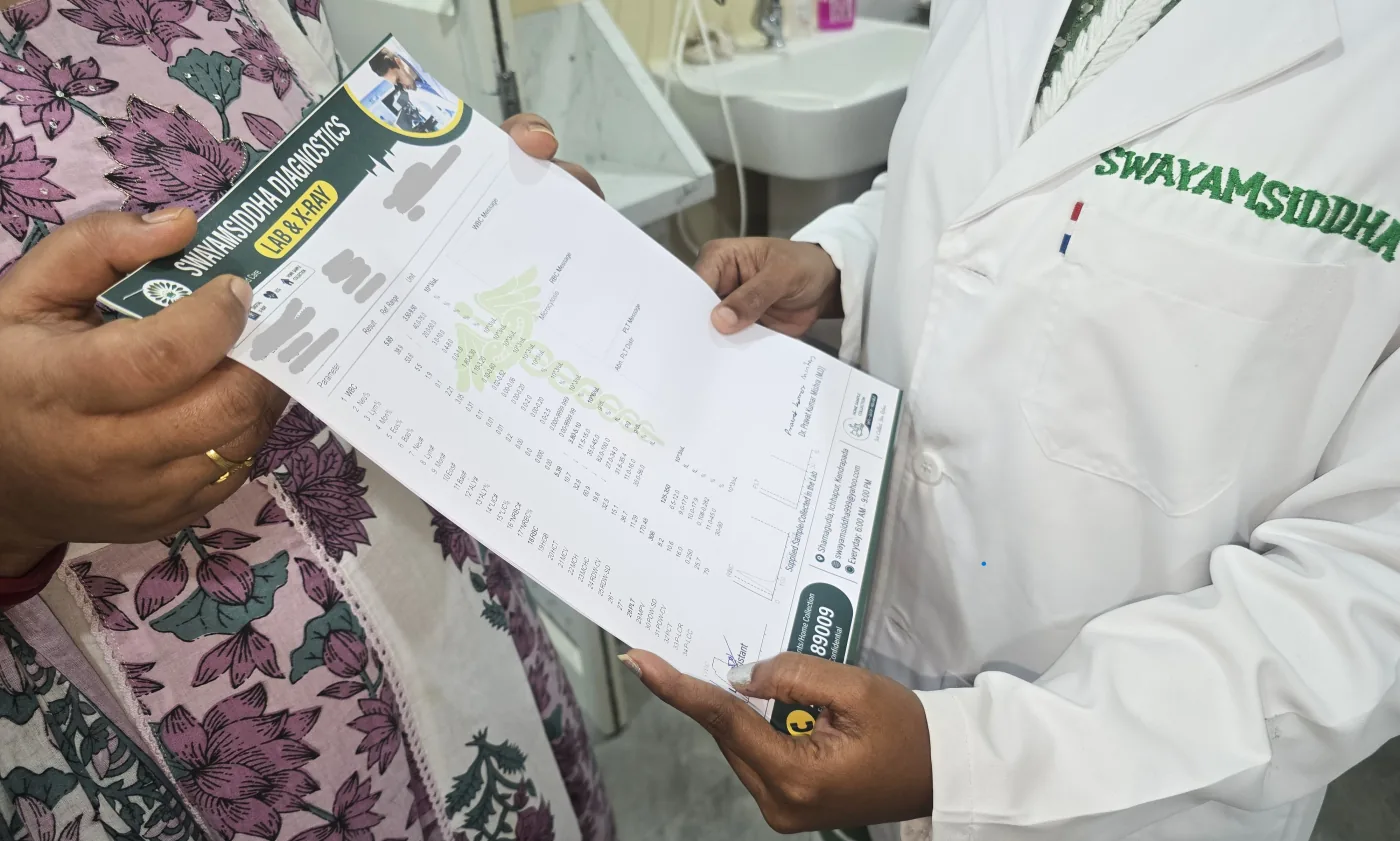 A printed Swayamsiddha Diagnostics report being handed across the counter